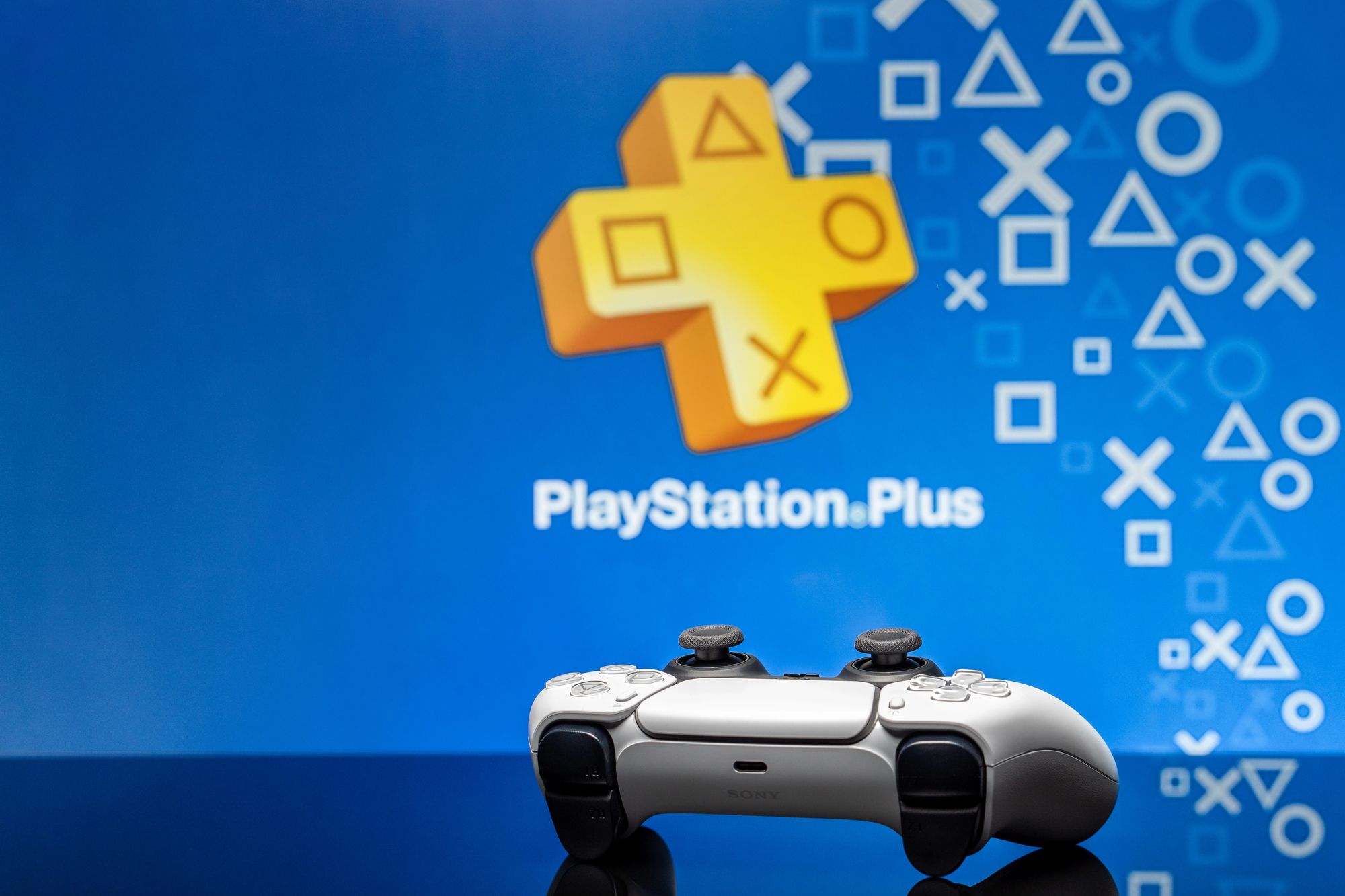 Геймпад DualSense на тлі інтерфейсу PlayStation Plus на телевізорі
